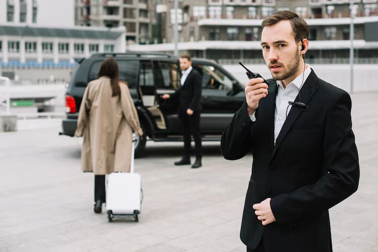 Chauffeur on a two-way radio while another driver assists a traveller with luggage