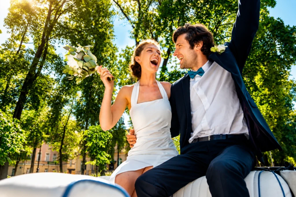 Happy bride and groom celebrating on a wedding car outdoors